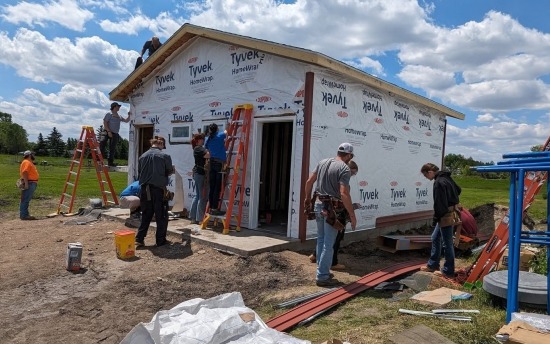 Several student construction workers at a Herdina Construction Camp, around a small structure they're helping to build at the 2024 camp.
