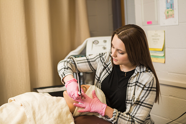 A cosmetology student with pink gloves works on a mannequin