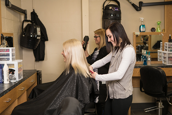 A cosmetology student cuts a blonde woman's hair