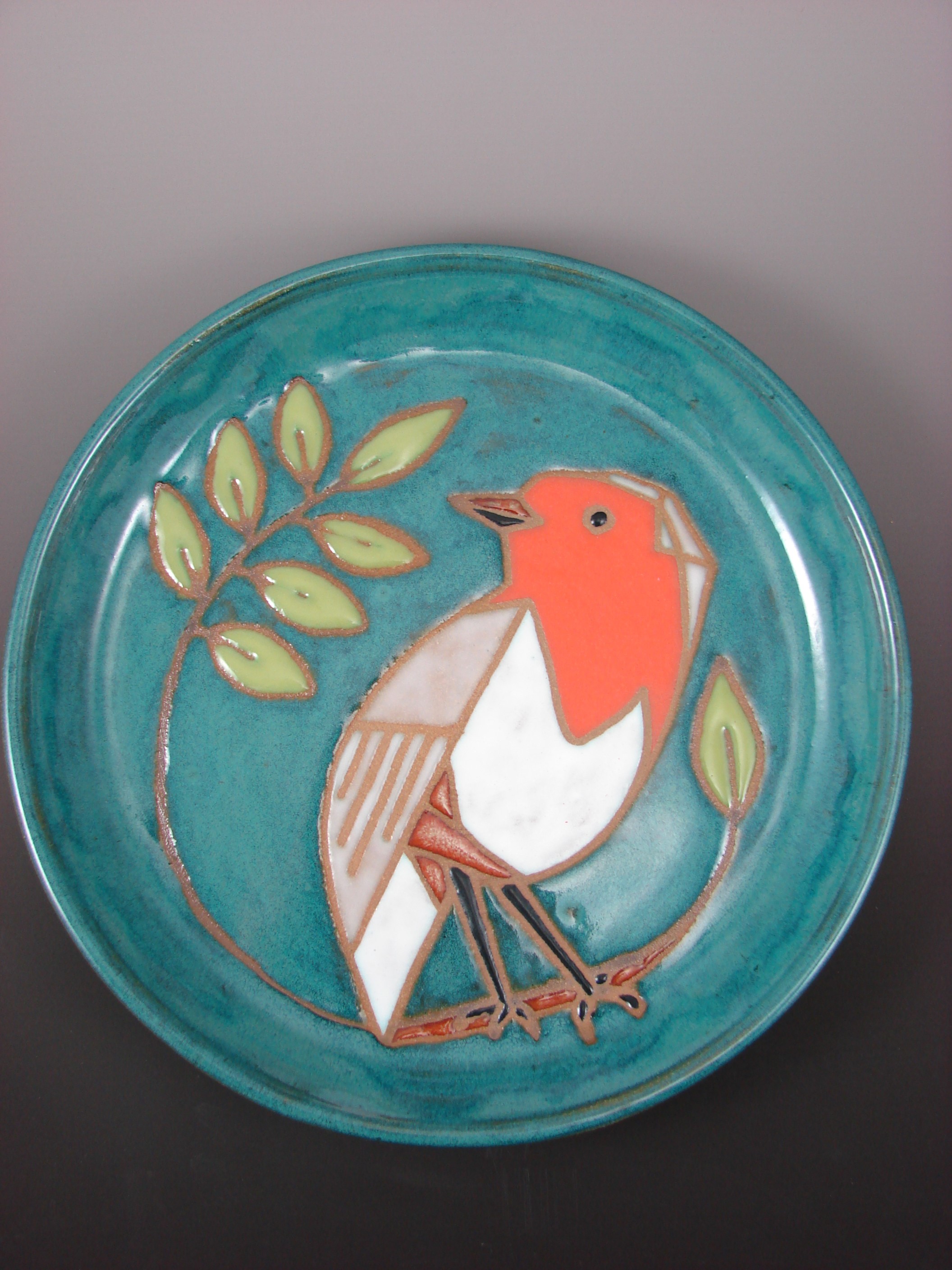 A blue-green ceramic plate featuring a robin perched on a branch