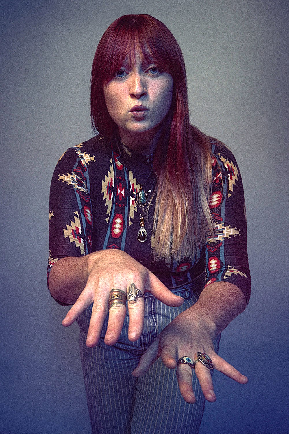 A woman with long red hair, Kaila Mullady, holds her hands out like a DJ spinning records.