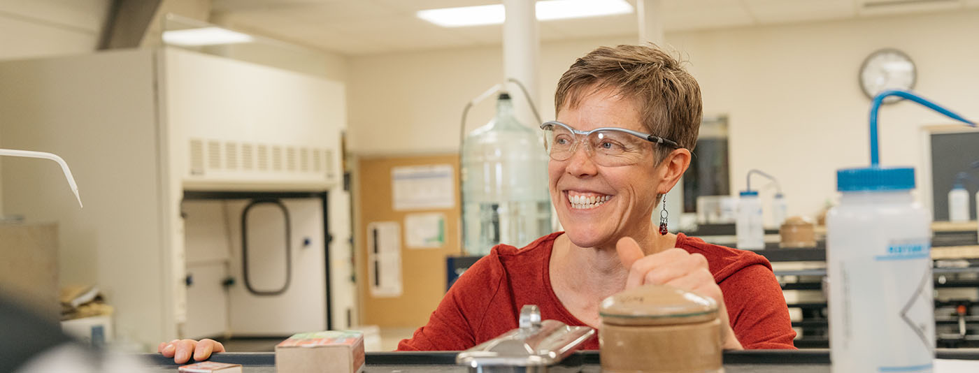 A lab instructor in a red shirt wears safety glasses