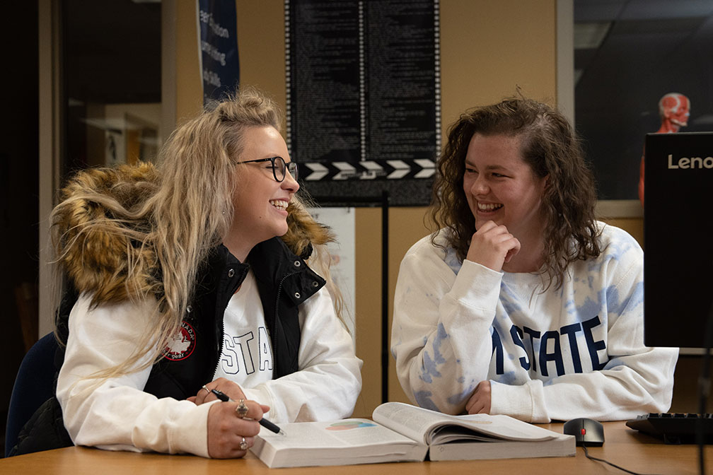 Two students seated at a table, laughing