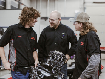 Kent Reisenauer and two PowerSports Technology students laugh during a class in the early 2020s.