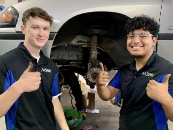 Fix It Forward volunteers give the thumbs up next to a car they fixed up for someone in need