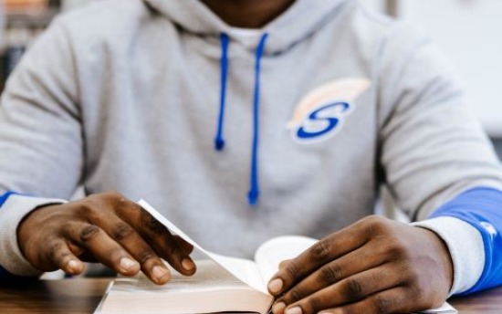 A student in a Spartans hoodie reads a book at the M State Fergus Falls library