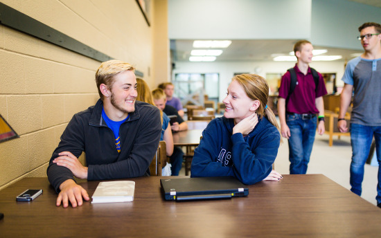 Students seated at a table at M State smile at each other