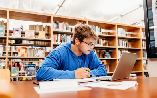 man in library sitting at table working at computer