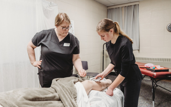 A massage therapy student and her instructor practicing massaging a leg