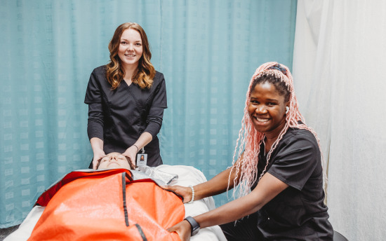 Two massage therapy students have another student laying on a massage bed while practicing their technique