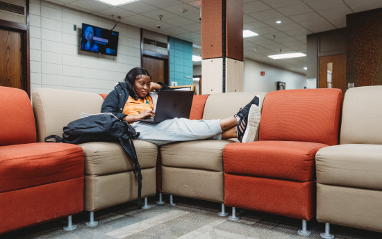 Photo of a student lounging on her laptop in the commons