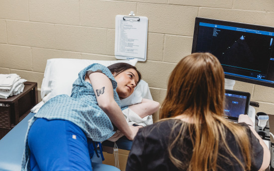 a person is laying on a bed while another person is looking at a monitor