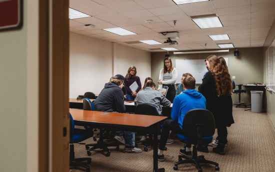 Several students gathered around a table where the instructor is showing blueprints in the architectural drafting and design course