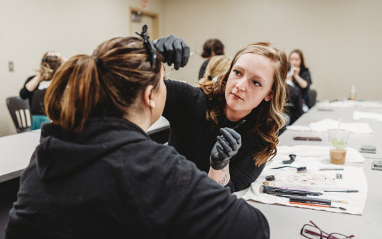 A cosmetology student is practicing makeup application on another student