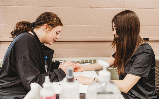 A student is practicing a manicure on another student