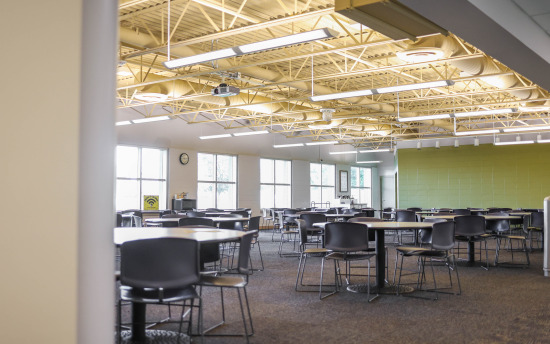 An empty cafeteria with large windows and many tables and chairs