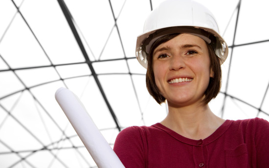 A person in a red sweater and white hard hat holds rolled-up papers