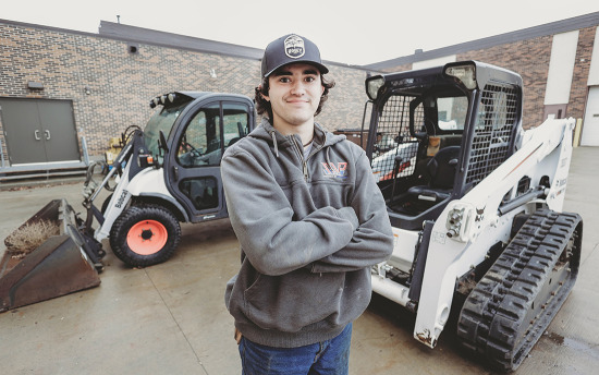  A student stands in front of heavy equipment outside M State