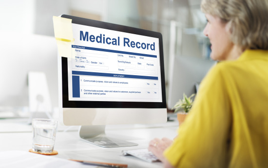 A person in yellow examines medical records on a computer monitor