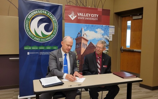 Two leaders from M State and VCSU sit down at a table to review an agreement between the two schools at a press conference on M State's Moorhead campus.