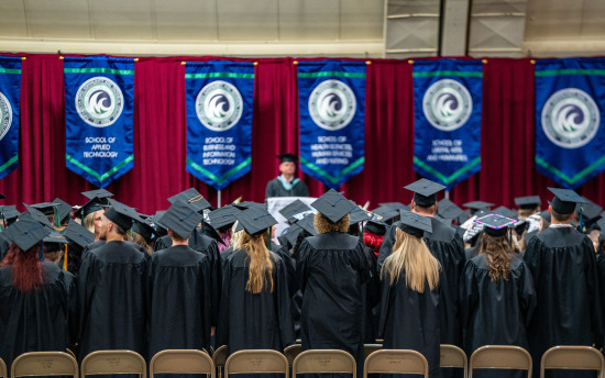 M State graduates, seated in long rows and adorned in their caps and gowns, listen to a speaker at a spring 2025 commencement ceremony.