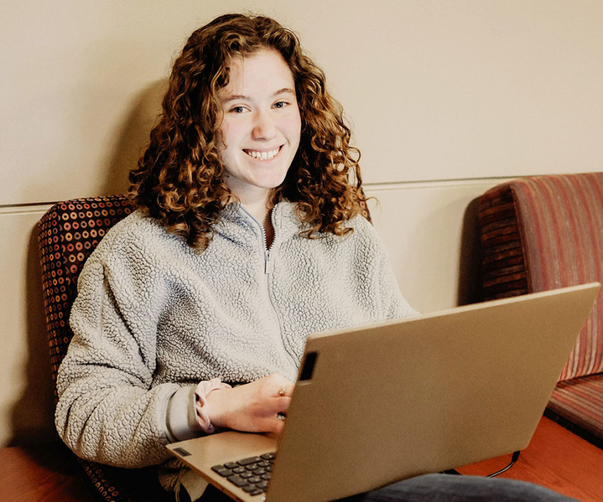 A seated student with a laptop smiles