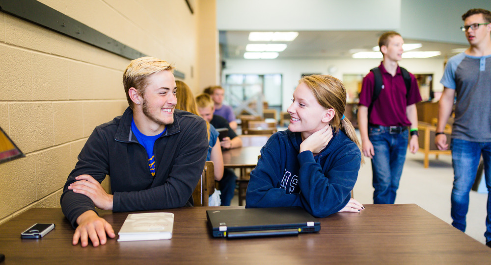 Students seated at a table at M State smile at each other